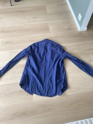 Mörkblå skjorta med knappar - Snygg mörkblå skjorta med klassisk krage och knäppning framtill. Skjortan har lång ärm och är tillverkad i ett mjukt bomullstyg som känns skönt mot huden. Perfekt för dig som gillar en enkel men stilren look. Slim Fit