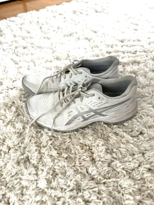 Vita Asics sneakers - Snygga vita sneakers från Asics med klassisk logga i silver på sidan. Skorna har lågt skaft, ovandel i ventilerande mesh och snörning framtill. Yttersulan är i slitstark gummi med bra grepp. Perfekta för dig som tränat eller går! 