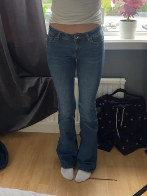 Blå bootcut jeans med midwaist midja - Säljer ett par klassiska blå bootcut jeans med hög midja och femficksmodell. Jeansen har en snygg tvätt och utsvängda ben, perfekta till sneakers eller boots. Materialet är stretchigt denim för skön passform. Passar dig som gillar retrovibbar och tidlös stil. Innerbenslängd 78, midjemått 34
