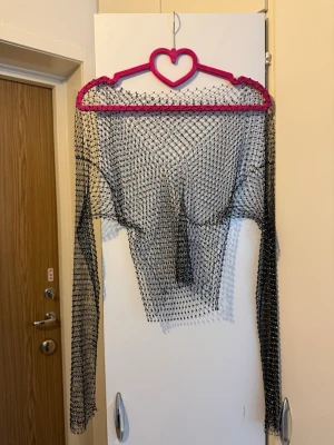 Svart topp med strass stenar strl S - Svart topp med långa ärmar. Toppen är i ett nätliknande material med strass stenar som skapar en glittrig effekt. Den har en rund halsringning och en figurnära passform.