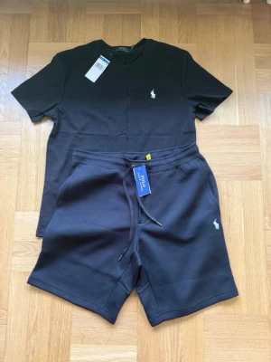 Ralph Lauren svart set t-shirt & shorts – storlek M - Ett jättefint och stilrent matchande sommarset från Ralph Lauren med en kortärmad t-shirt och tillhörande shorts i klassiskt svart utförande. Perfekt och bekvämt set för varma dagar eller som lounge-wear. ✔ Helt nytt och aldrig använt ✔ Storlek: M ✔ Märke: Ralph Lauren ✔ Färg: Svart ✔ Skönt och följsamt material i hög kvalitet 📩 Skicka ett meddelande vid frågor eller prisförslag! 🛍 Lägg till i en bundle för att spara upp till 20% rabatt! 📦 Garanterad leverans samma eller nästa dag 🌟 