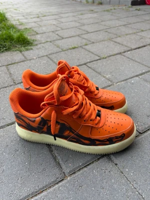 Nike Air Force 1 orange sneakers - Säljer ett par Nike Air Force 1 sneakers i en riktigt fet orange färg med svarta detaljer och mönster längs sidorna. Skorna är i riktigt bra skick och bara andvända fåtal gånger. Kostar 1999kr ny. Billigare vid snabb affär!