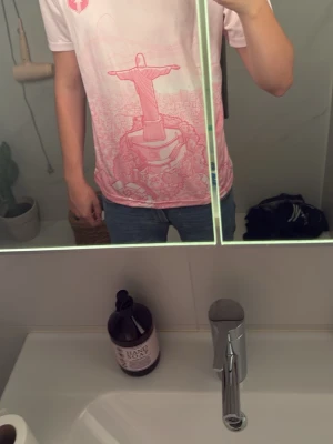 Rosa Nike t-shirt  - Säljer en ljusrosa t-shirt från Nike med ett stort tryck av Kristusstatyn i Rio de Janeiro på framsidan. T-shirten har korta ärmar, rund hals och en sportig vibe. Perfekt för dig som gillar unika prints och streetwear.