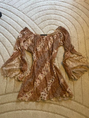 Bohemisk blommig offshoulder blus - Säljer en bohemisk offshoulder blus från Vila i tunnt, transparent tyg. Blusen har ett brunt och beige blommönster med inslag av vitt och rött, samt vida, fladdriga ärmar. Perfekt för dig som gillar romantisk och avslappnad stil. Superfin❤️