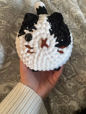 Virkad katt plushie svartvit - Supergullig handgjord virkad katt plushie i svart och vitt med stora plastögon och broderad nos och mun. Tillverkad i mjukt garn och har en rund form med liten svans. Gjord av mig!