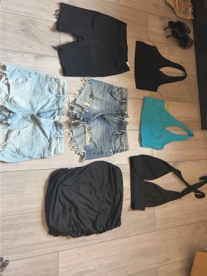 Svarta och jeansshorts i olika stilar - Tre par shorts: ett par svarta, ett par ljusblå slitna jeansshorts och ett par mörkblå slitna jeansshorts. Alla har råa kanter och klassisk femficksdesign. Perfekta för sommaren och avslappnade dagar.