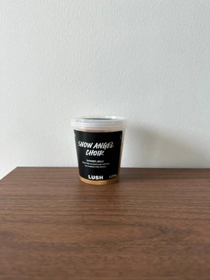 Lush Snow Angel Choir Shower Jelly - Unik duschjelly från Lush i doften Snow Angel Choir som luktar super milk. Kommer i en genomskinlig plastburk med svart etikett och vitt lock. Innehållet är guldigt och geléaktigt, perfekt för dig som vill ha en rolig twist på duschrutinen. Förpackningen är oöppnad 