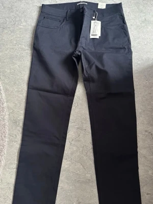 Svarta slim fit jeans - Snygga svarta slim fit jeans med klassisk femficksdesign och normal midja. Jeansen har raka ben och är tillverkade i ett mjukt bomullsmaterial med lite stretch för extra komfort. Perfekta för en stilren och enkel look.