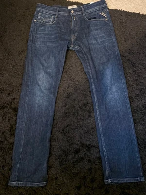 Mörkblå raka jeans från Replay - Säljer ett par mörkblå jeans från Replay med raka ben och klassisk femficksmodell. Jeansen har snygga kontrastsömmar och en liten logotypdetalj på bakfickan. Tillverkade i slitstarkt denimtyg som ger en tidlös look.
