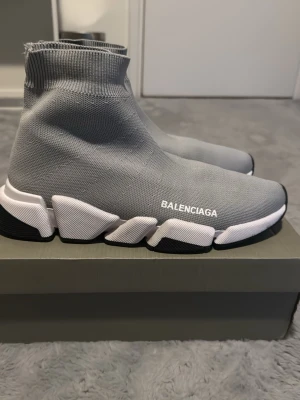 Grå Speed Trainer sneakers - Gråa Speed Trainer sneakers med stickad ovandel i textil och vit logga på sidan. Skorna har en chunky vit och svart sula med grafiska detaljer och en strumpliknande passform som sitter tight runt ankeln. Perfekt för dig som gillar en modern och sportig look. Box följs även med!📦SKICKAR DAGEN DU KÖPER!!!