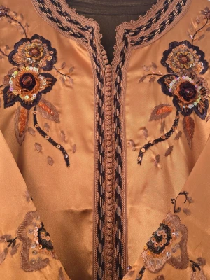 Guldig långklänning med broderi - Unik långklänning i guldigt satinliknande material med detaljerade blommiga broderier och paljetter framtill. Klänningen har långa ärmar och vacker dekorerad kant längs urringningen och öppningen. Perfekt för dig som vill sticka ut med elegans.