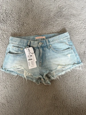 Ljusblå jeansshorts från Gina Tricot - Snygga ljusblå jeansshorts från Gina Tricot med fransiga kanter och klassisk femficksmodell. Shortsen har låg midja och slitna detaljer framtill för en avslappnad look. Perfekta för varma sommardagar.