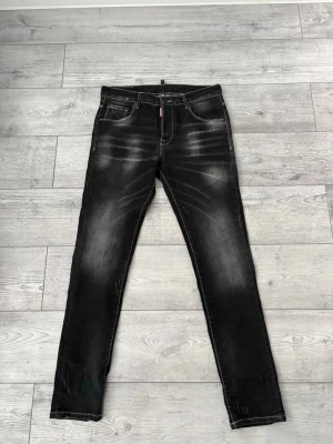 Svarta skinny jeans med slitningar dsquared2 - Säljer ett par svarta skinny jeans med snygga slitningar och tvättade detaljer. Klassisk femficksmodell med dragkedja och knapp. Jeansen har en modern, smal passform och cool faded effekt på låren och knäna.                                                   Jag är 180cm lång och dom passar mig perfekt