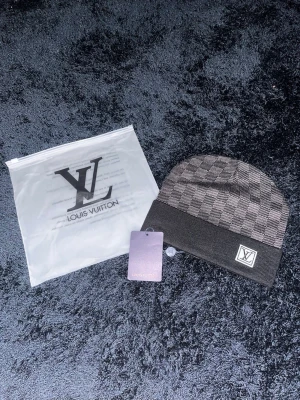 L.V mössa - Snygg gråmelerad mössa från L. V med klassiskt rutmönster och vikt kant. L. V-logga framtill på en patch. Perfekt accessoar för dig som vill ha en exklusiv touch till din outfit.
