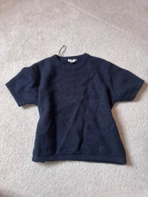 Mörkblå stickad t-shirt från Gina Tricot - En enkel och stilren mörkblå stickad t-shirt från Gina Tricot. T-shirten har korta ärmar, rund halsringning och är gjord i ett mjukt, stickat material som känns skönt mot huden. Perfekt för en avslappnad och trendig look.