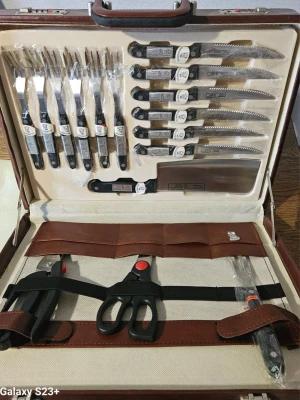 Bestick- och knivset i väska - Säljer ett komplett bestick- och knivset i en brun väska. Innehåller flera knivar, gafflar, sax, tång och köttyxa med svarta handtag och detaljer i rostfritt stål. Perfekt för köket eller grillkvällen, allt snyggt organiserat i fodralet.