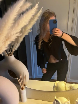 Svart croppad omlottopp med vida ärmar - Snygg svart croppad omlottopp med v-ringning och vida, utsvängda ärmar. Toppen har en trendig och ungdomlig look, perfekt för dig som vill sticka ut. Materialet känns mjukt och följsamt mot kroppen. Storlek m men skulle säga att den är S