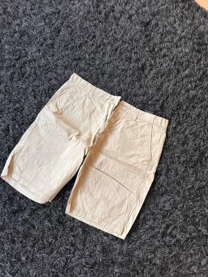 Beige bomullsshorts med fickor - Säljer ett par klassiska beige shorts i bomull med raka ben och praktiska sidfickor. Perfekta för varma dagar och enkel att matcha med olika stilar. Passar dig som gillar en clean och avslappnad look.