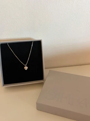 Silverhalsband med hjärthänge från Safira - Ett stilrent silverhalsband från Safira med ett litet hjärthänge. Kedjan är tunn och elegant, perfekt för att ge en söt touch till din outfit. Levereras i originalask.