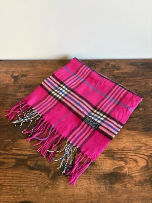 Burberry Halsduk - Vintage Burberrys halsduk i 100% lambswool. Made in England. Klassisk check i mörkare/bruna toner med diskret och tidlös look. Väldigt bra skick med endast mindre tecken på användning. Perfekt för en clean casual/old money stil.