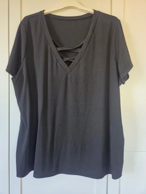 Svart t-shirt med v-ringning och band - Svart t-shirt med v-ringning och dekorativa band framtill. Modellen är loose fit med korta ärmar och mjukt material, perfekt för en avslappnad stil. Enkel men ändå med en snygg detalj vid halsen.