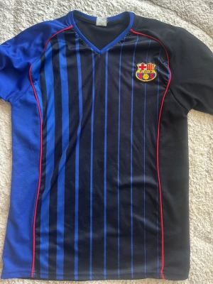FC Barcelona matchtröja blå/svart - Snygg FC Barcelona matchtröja i svart och blått med tunna vertikala ränder och röda detaljer. Tröjan har klubbmärket på bröstet och är tillverkad i ett lätt och snabbtorkande material, perfekt för fotbollsträning eller sport. Pris kan diskuteras privat 