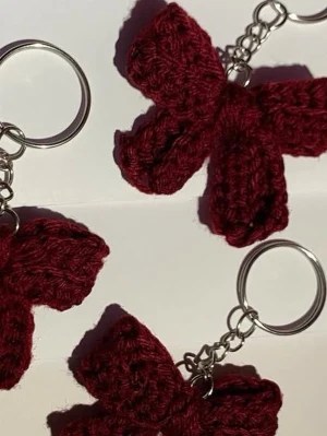 Handgjord vinröd rosett nyckelring - Säljer en söt handvirkad nyckelring med vinröd rosett. Rosetten är gjord i garn och sitter fast på en klassisk metallring med kedja. Perfekt accessoar till nycklar eller väska.