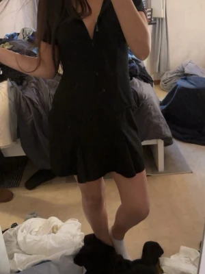 Svart kort klänning med dragkedja - Snygg svart kortklänning med v-ringning och dragkedja framtill. Klänningen har en lätt utsvängd kjol och korta ärmar. Perfekt för dig som gillar en enkel men stilren look.