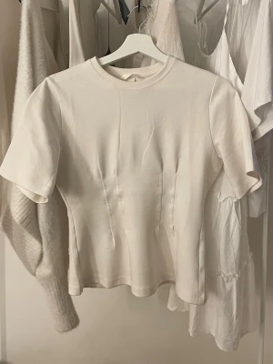 Vit t-shirt med figurnära passform - Snygg vit  t-shirt med rund hals och korta ärmar. Modellen är figurnära och enkel i designen, perfekt att matcha med olika outfits. Tillverkad i mjukt bomullsmaterial för en skön känsla. Knappt använd, storlek xs/s💕
