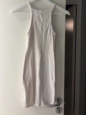 Vit ribbad klänning från Pull&Bear - Säljer en vit ribbad kortklänning från Pull&Bear. Klänningen är ärmlös med smala axelband och har en enkel, rak passform. Perfekt för varma dagar och enkel att styla med sneakers eller sandaler.