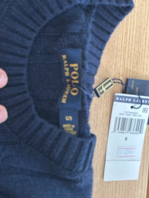 Mörkblå kabelstickad tröja Polo Ralph Lauren - Säljer en ny mörkblå tröja från Polo Ralph Lauren med rund halsringning och ribbade muddar. Klassisk och stilren design i mjukt material, perfekt för lager-på-lager. Tröjan är i storlek s. Säljer för att den inte passade mig.