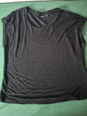 Svart t-shirt från Crivit - En enkel svart t-shirt från Crivit med rund hals och korta ärmar. Perfekt basplagg i garderoben, lätt att matcha och skön att bära. Tillverkad i mjukt material som känns bekvämt mot huden.