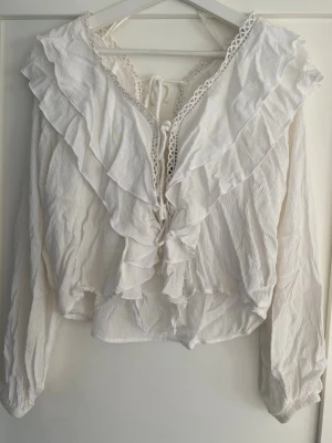 Vit volangblus med knytning - Superfin vit blus med volanger och knytning framtill. Den har en liten öppen rygg som är fint nu i vår💕💕jag ber så hemsk mycket om ursäkt för att den ser så skrynklig ut på bilden!!