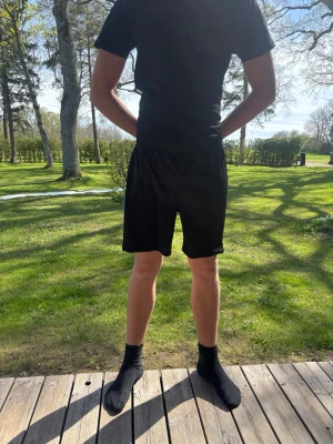 Svarta träningsshorts i polyester - Svarta shorts med elastisk midja, perfekt för träning eller chill. De är tillverkade i ett lätt och smidigt polyestermaterial som andas bra. Klassisk rak passform och enkel design utan synliga loggor eller detaljer.