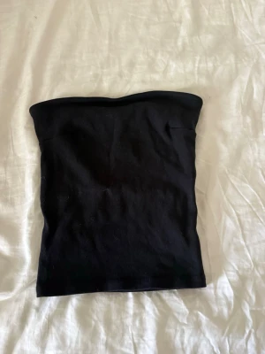 Svart tubtopp från Gina Tricot - En svart, enkel och stilren tubtopp från Gina Tricot. Toppen är axelbandslös och har en tight passform som sitter snyggt på kroppen. 