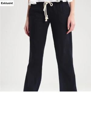 Svarta linnebyxor med dragsko - Snygga svarta linnebyxor med avslappnad passform och vit dragsko i midjan. Perfekta för en chill och stilren look. Byxorna har raka ben och är tillverkade i ett lätt och luftigt linnematerial.