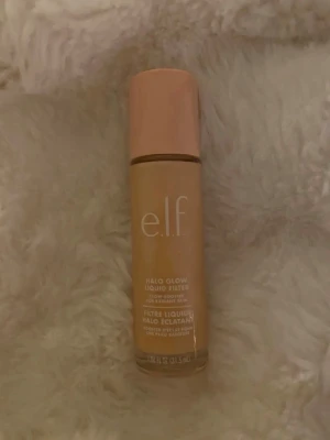e.l.f. Halo Glow Liquid Filter foundation - Foundation från e.l.f. i färgen Halo Glow Liquid Filter. Kommer i en cylinderformad flaska med beige nyans och rosa lock. Perfekt för dig som vill ha en naturlig glow och jämn hudton. Flaskan är gjord av plast och har tydlig märkning på framsidan.