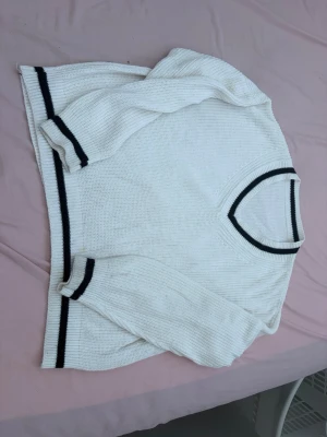Vit stickad tröja med svarta ränder - Vit stickad tröja med svarta ränder vid halsringning, ärmslut och nederkant. Tröjan har en avslappnad passform och är tillverkad i ett mjukt material. Perfekt för en stilren och enkel look.