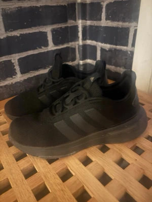 Svarta Adidas sneakers med mesh - Svarta sneakers från Adidas med klassiska tre ränder på sidan. Ovandelen är i meshmaterial för bra andningsförmåga och skon har en chunky sula. Låg modell med snörning och diskret Adidas-logga på plösen. Perfekta för en sportig och stilren look.