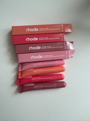 Rhode Peptide Lip Tint läppbalsam - Flera Rhode Peptide Lip Tint läppbalsam i olika nyanser som rosa, nude, röd, orange och brun. Tubformade balsam med färgade förpackningar som matchar nyansen. Perfekt för dig som vill ha återfuktade läppar med en hint av färg. Oanvänd, endast öppnade förpackningar för att visa att de faktiskt finns!