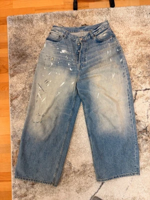 Acne 2023m - Säljer ett par blåa wide leg acne studios 2023m repliker jeans med coola slitningar och blekta detaljer framtill. Jeansen har hög midja, klassisk femficksdesign och stängs med knapp och dragkedja. Perfekta för en avslappnad streetstil.
