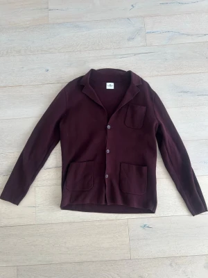 Vinröd kofta/overshirt från John Henric  - Vinröd kofta/overshirt från John Henric med tre knappar framtill, klassisk krage och tre praktiska fickor. Rak passform och lång ärm. Perfekt för lager-på-lager och enkel att styla till olika outfits.