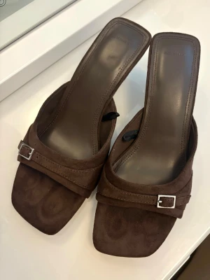 Klackar i nyskick🤎 - Snygga bruna sandaler från Bershka med fyrkantig tå och låg klack. Ovandelen är i mockaimitation med dekorativt spänne i silver. 