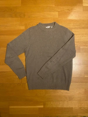 Grön stickad tröja från Dobber - En stilren beige stickad tröja från Dobber i storlek M. Tröjan har rund halsringning, långa ärmar och ribbstickade muddar vid ärmslut och nederkant. Perfekt för lager-på-lager och enkel att matcha med jeans eller chinos.