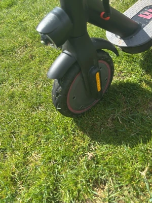 Svart elscooter med röda detaljer - Elektrisk scooter i svart med röda detaljer på hjulen och reflexer på framgaffeln. Scootern har bred fotplatta, framlykta och robusta däck. Perfekt för att ta sig fram snabbt i stan eller till skolan.