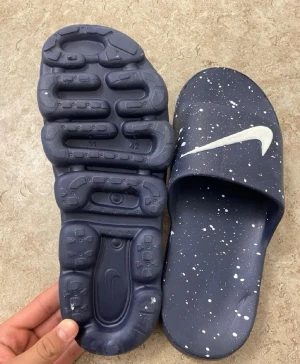 Blå Nike sandaler med vit stänkmönster - Snygga blå sandaler från Nike med vit stänkmönster och klassisk vit swoosh-logga. Sandalerna har en chunky sula med unik struktur undertill och bred rem över foten. Tillverkade i ett lätt och bekvämt syntetmaterial som passar perfekt för chill dagar.