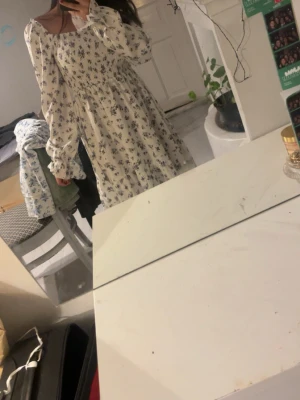 Vit blommig långklänning med puffärm - Romantisk vit långklänning med blått blommönster och smockad överdel. Klänningen har långa puffärmar och en söt, rynkad kant vid halsen. Perfekt för vår och sommar, med en luftig och flowy känsla. Aldrig använd, köptes på plick helt oanvänd och ny men fanns dock ingen lapp på den, skulle vilja gissa på boohoo 💕