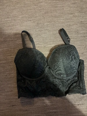 Svart spets-bh med vadderade kupor - Snygg svart bh med vadderade kupor och spetsdetaljer. Justerbara axelband och bredare band under bysten för extra stöd. Perfekt för dig som gillar en feminin och stilren look.