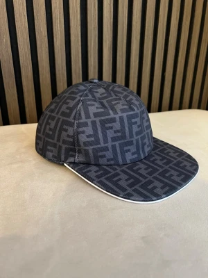 Svart keps med F logga - Snygg svart keps från Fendi med ikoniskt FF-mönster över hela kepsen. Kepsen har böjd skärm med vit kant och justerbar rem baktill. Tillverkad i ett slitstarkt tyg som ger en exklusiv känsla. Perfekt accessoar för att lyfta din streetwear-stil.