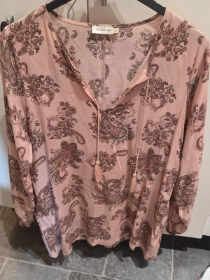 Rosa paisleymönstrad klänning  - Säljer en rosa klänning från lager157 paisleymönster i bruna toner. Klänningen har långa ärmar, v-ringning med snörning och är tillverkad i ett mjukt, lätt tyg. Perfekt för dig som gillar bohemisk stil och bekväma plagg.